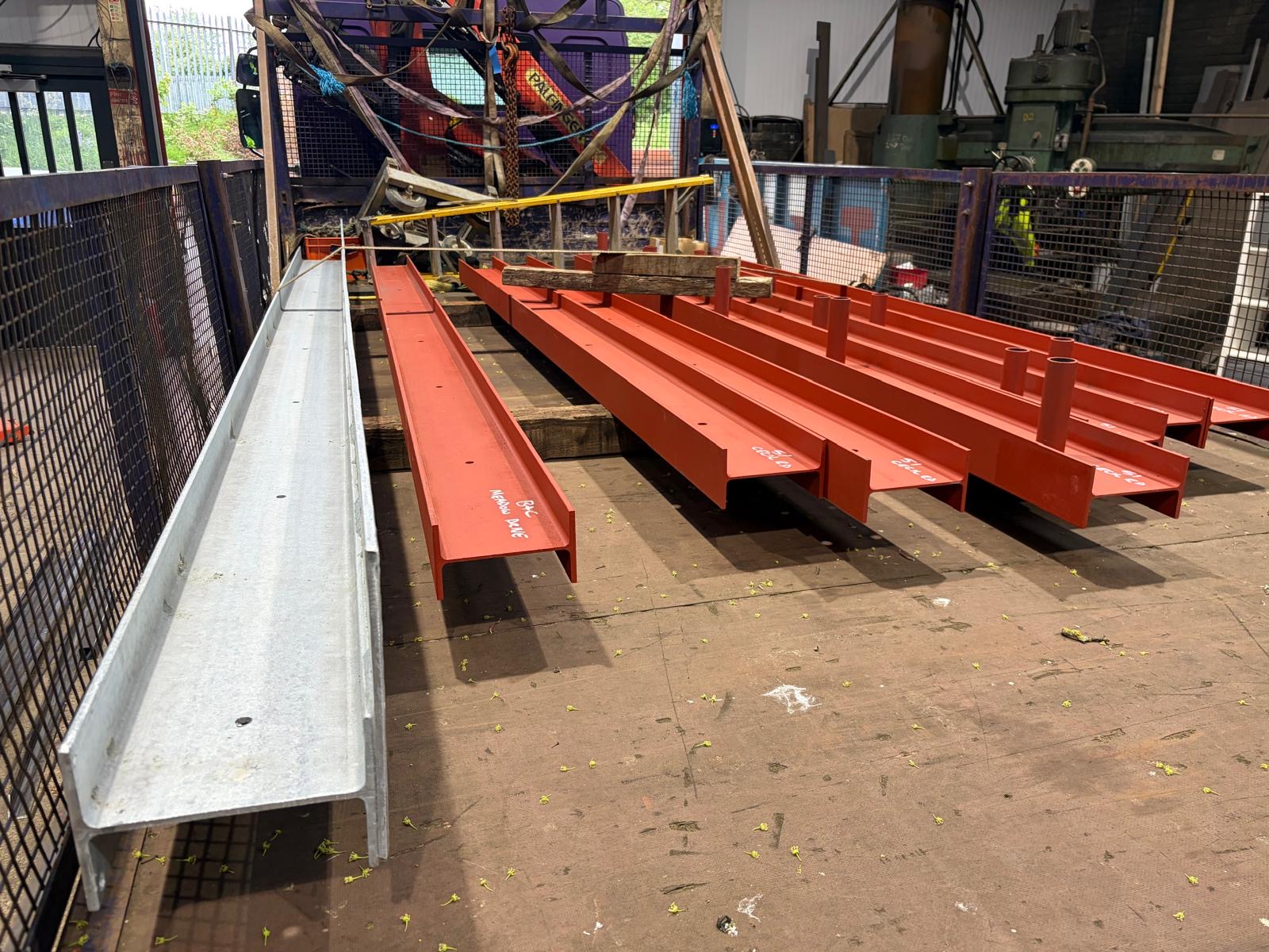 Mixed galvanised and red painted beams laid out in the workshop