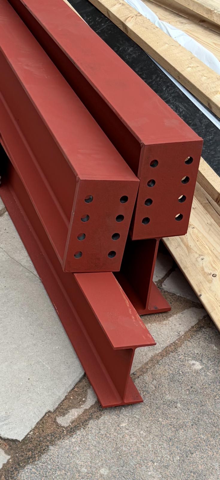 Red beams with drilled end plates ready for bolted assembly