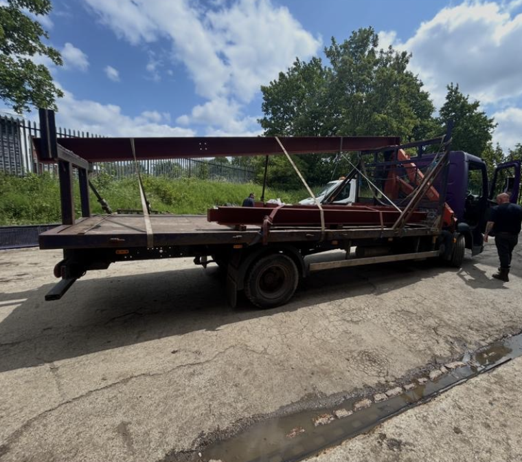 Red fabricated beams strapped onto a flatbed delivery truck