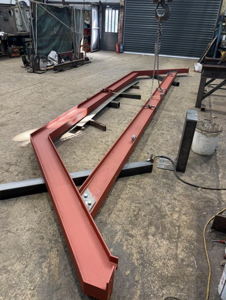 Fabricated red portal frame being lifted by chain hoist in the workshop
