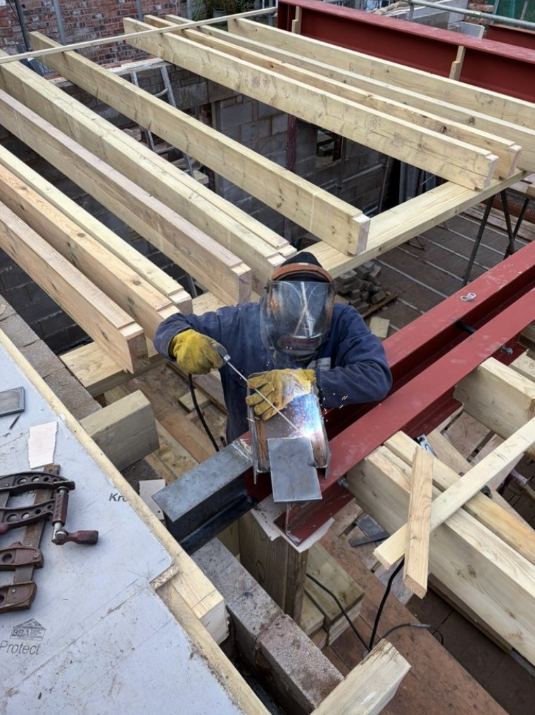 Welder fitting steelwork between timber floor joists on site